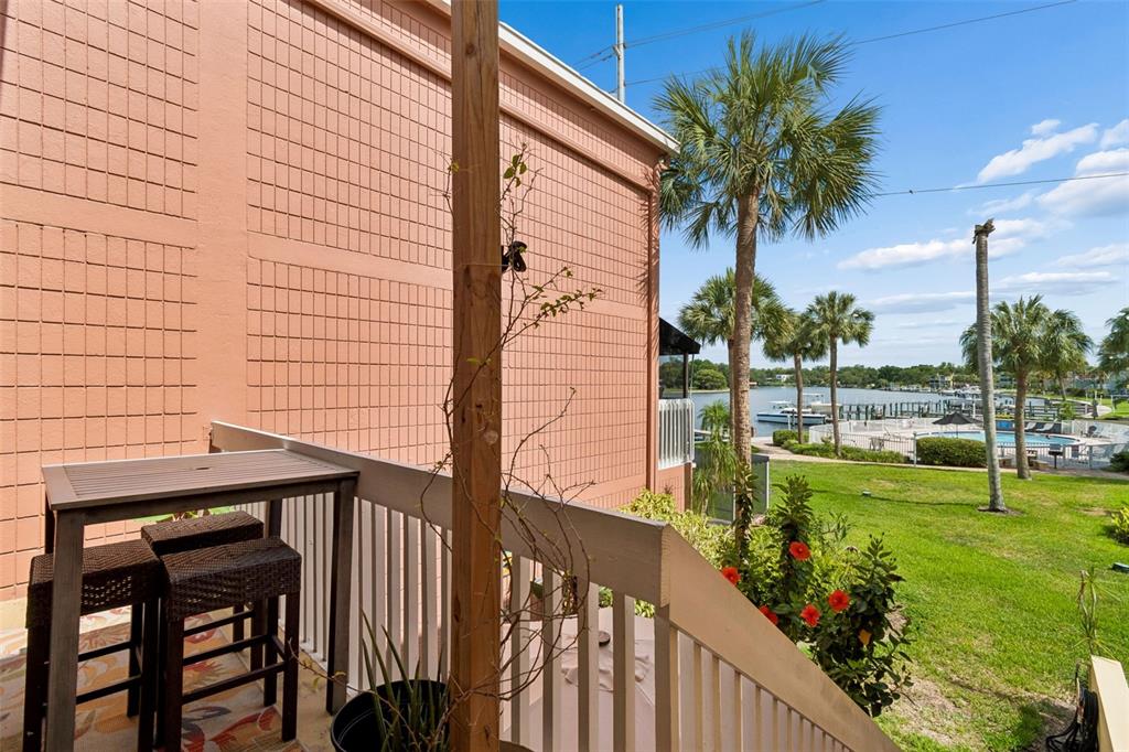 A balcony with a small table and chairs overlooks a grassy lawn and a canal — 2424 W TAMPA BAY BOULEVARD UNIT I204, TAMPA, FL