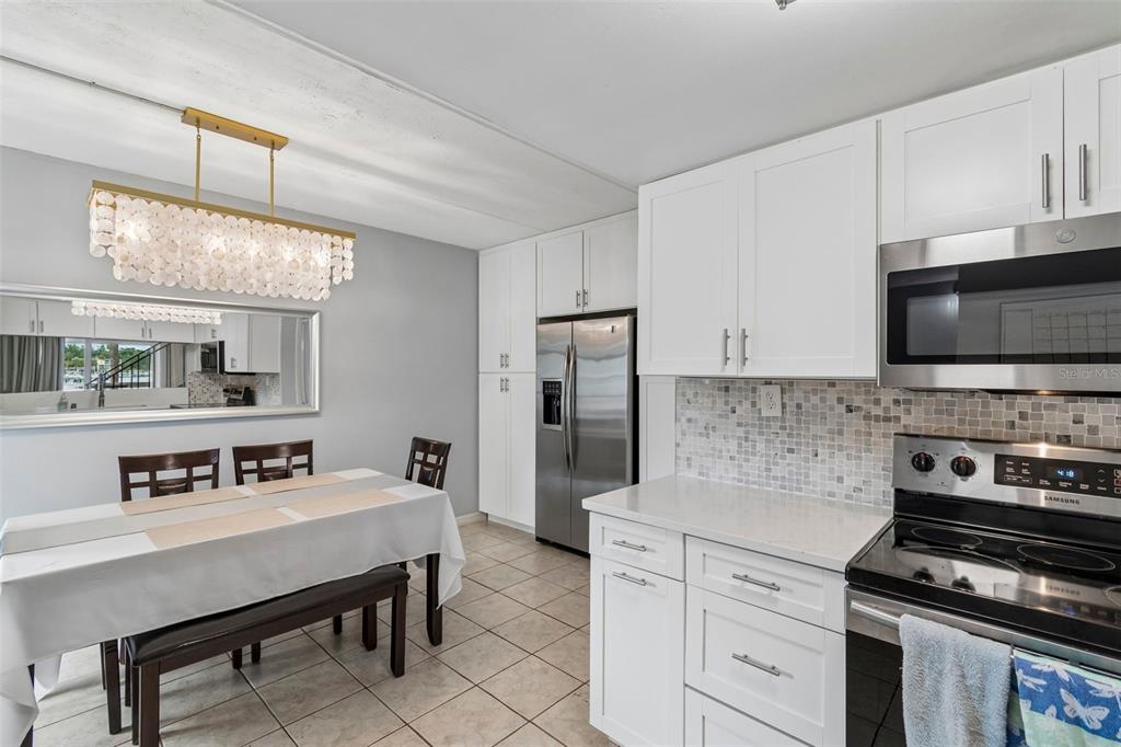 A kitchen and dining area with white cabinets, stainless steel appliances, and a shell chandelier — 2424 W TAMPA BAY BOULEVARD UNIT I204, TAMPA, FL
