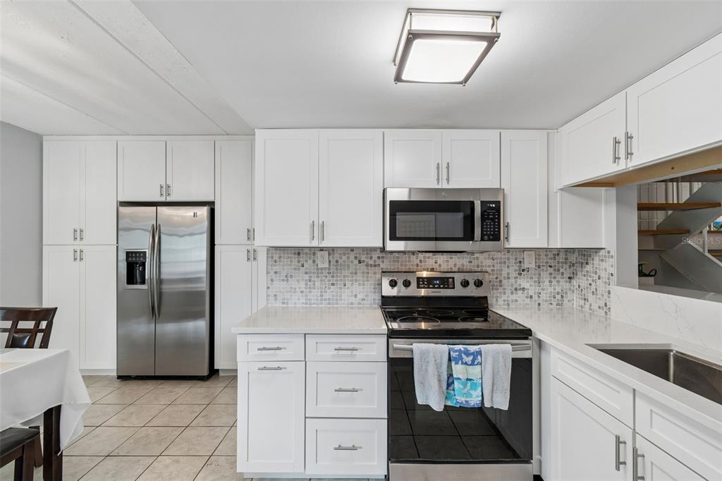 A kitchen features white cabinetry, stainless steel appliances, a mosaic backsplash, and light countertops — 2424 W TAMPA BAY BOULEVARD UNIT I204, TAMPA, FL