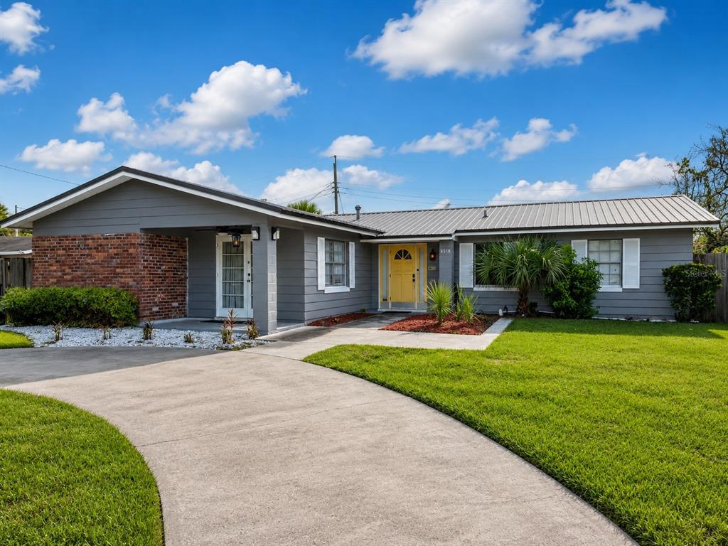 A single-story house with gray siding, a brick accent wall, and a yellow front door — 6518 VOLTAIRE DRIVE, ORLANDO, FL