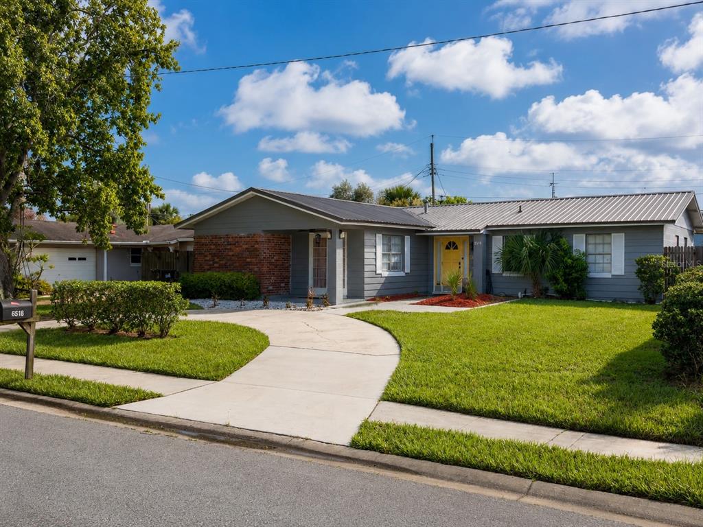 A single-story gray house with a metal roof, brick accent wall, and yellow front door — 6518 VOLTAIRE DRIVE, ORLANDO, FL