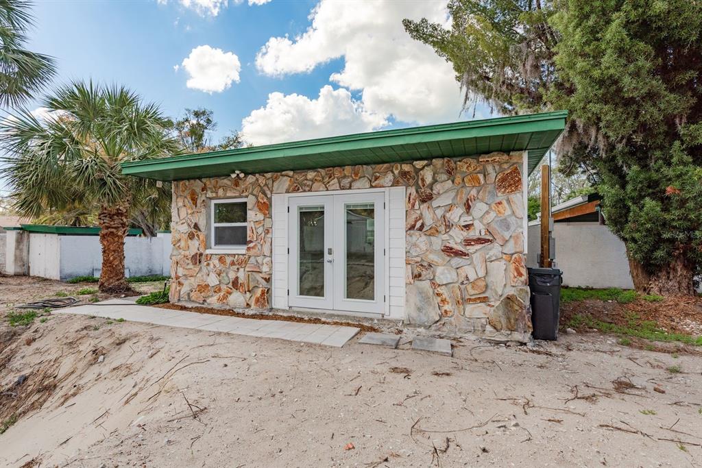 A small, stone-faced detached building with a green roof and white French doors — 1115 PENNSYLVANIA AVENUE, PALM HARBOR, FL