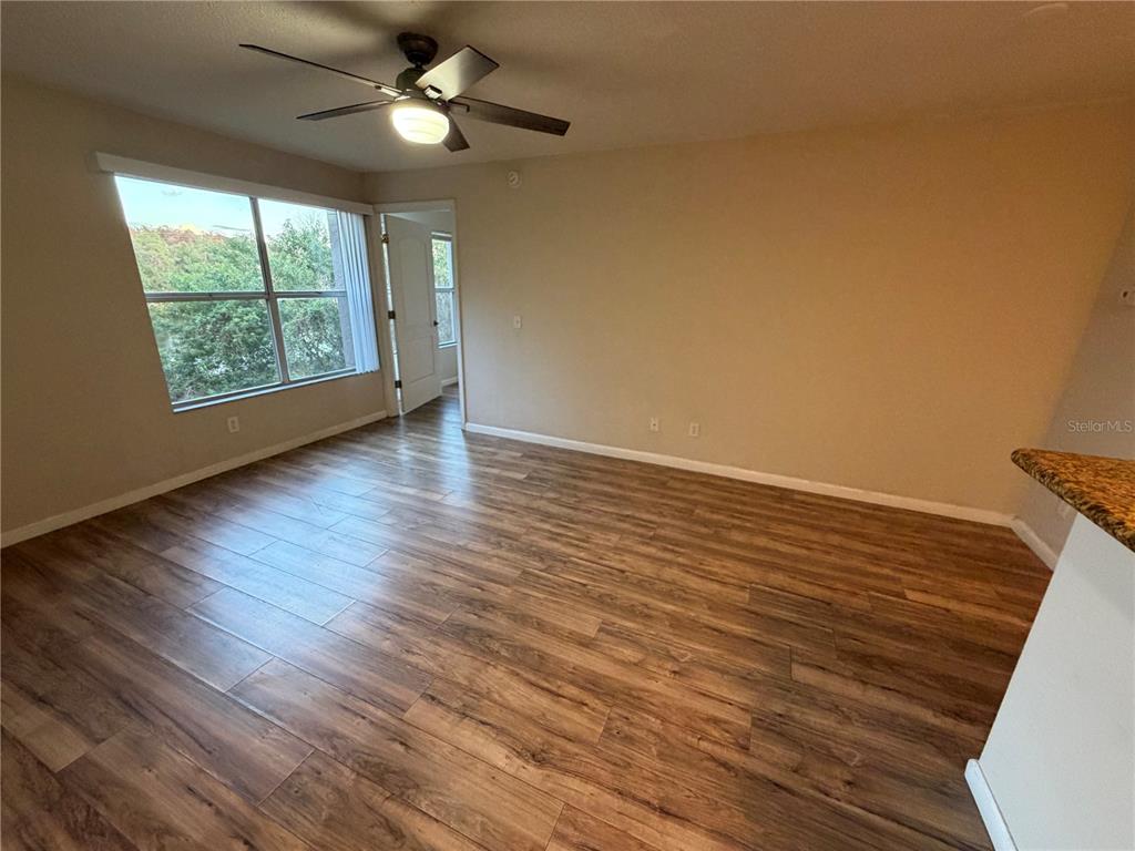 An empty room features wood-look flooring, a ceiling fan, and a window with outdoor views — 5128 CONROY ROAD UNIT 725, ORLANDO, FL