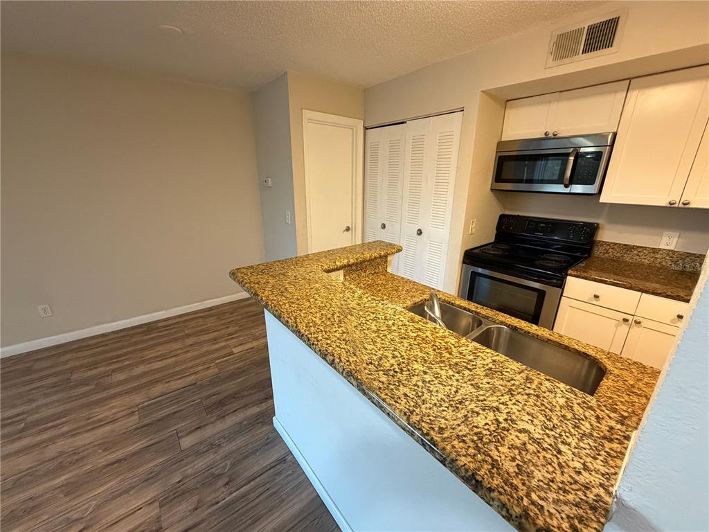 A kitchen features a granite breakfast bar, stainless steel sink, and white cabinetry — 5128 CONROY ROAD UNIT 725, ORLANDO, FL