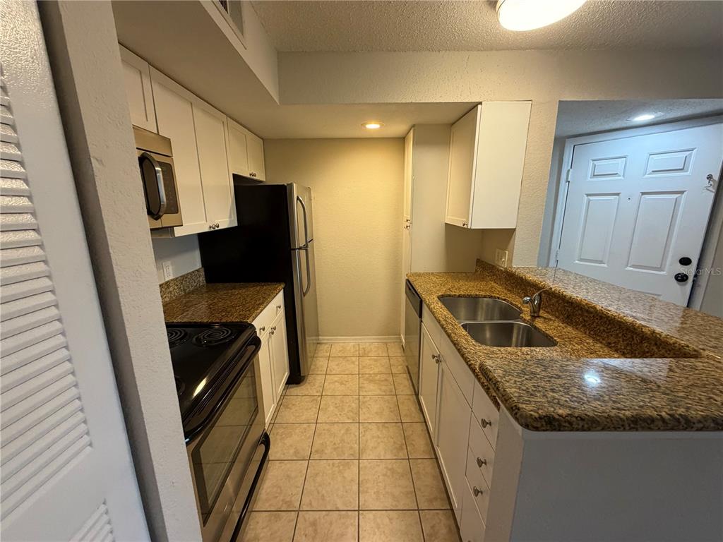 A galley kitchen features white cabinets, granite countertops, stainless steel appliances, and tile flooring — 5128 CONROY ROAD UNIT 725, ORLANDO, FL