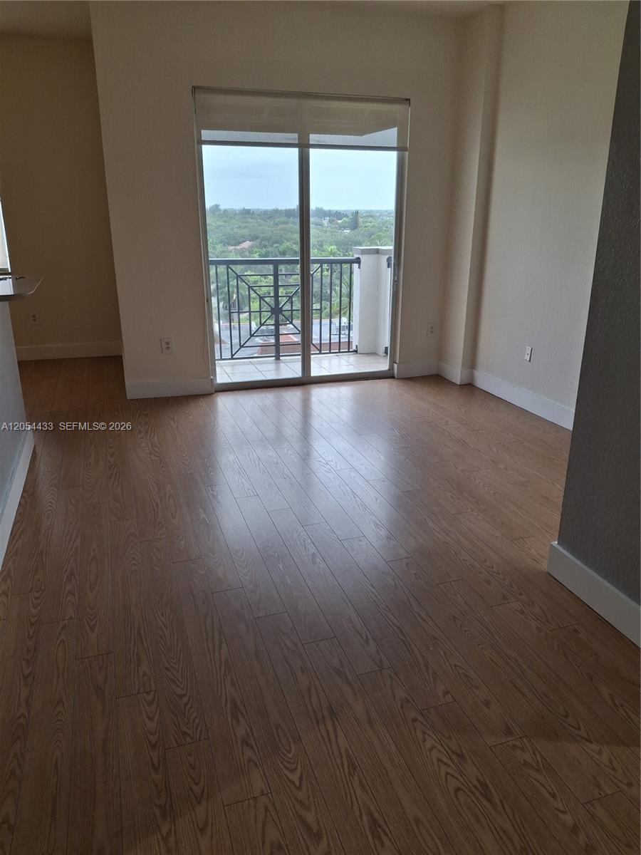 An empty room features light wood-look flooring, beige walls, and a sliding glass door to a balcony — 9021 SW 94th St, Miami FL 33176, MIAMI, FL