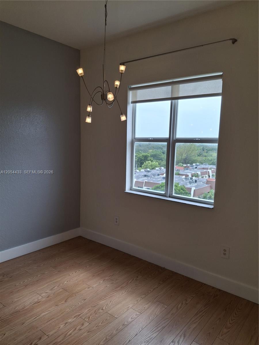 An empty room features wood-look flooring, a modern chandelier, and a window with exterior views — 9021 SW 94th St, Miami FL 33176, MIAMI, FL