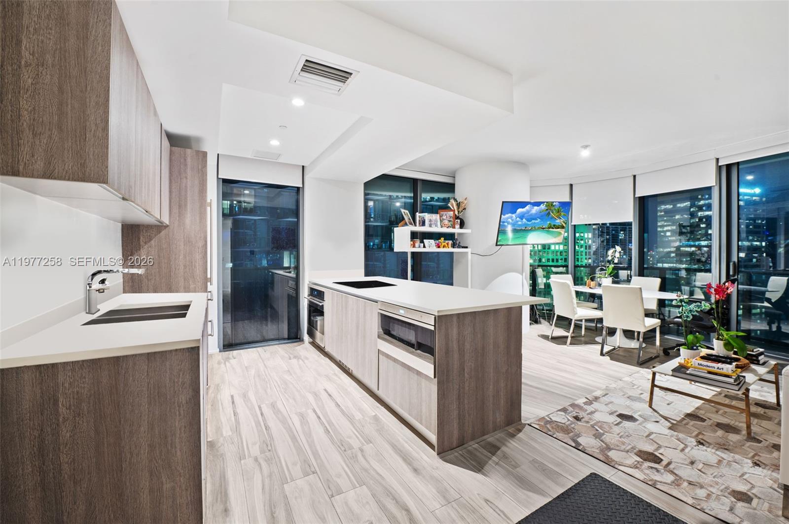A modern kitchen with wood-toned cabinetry and a central island overlooks a dining area — 801 S Miami Ave # 2705, Miami FL 33130, MIAMI, FL