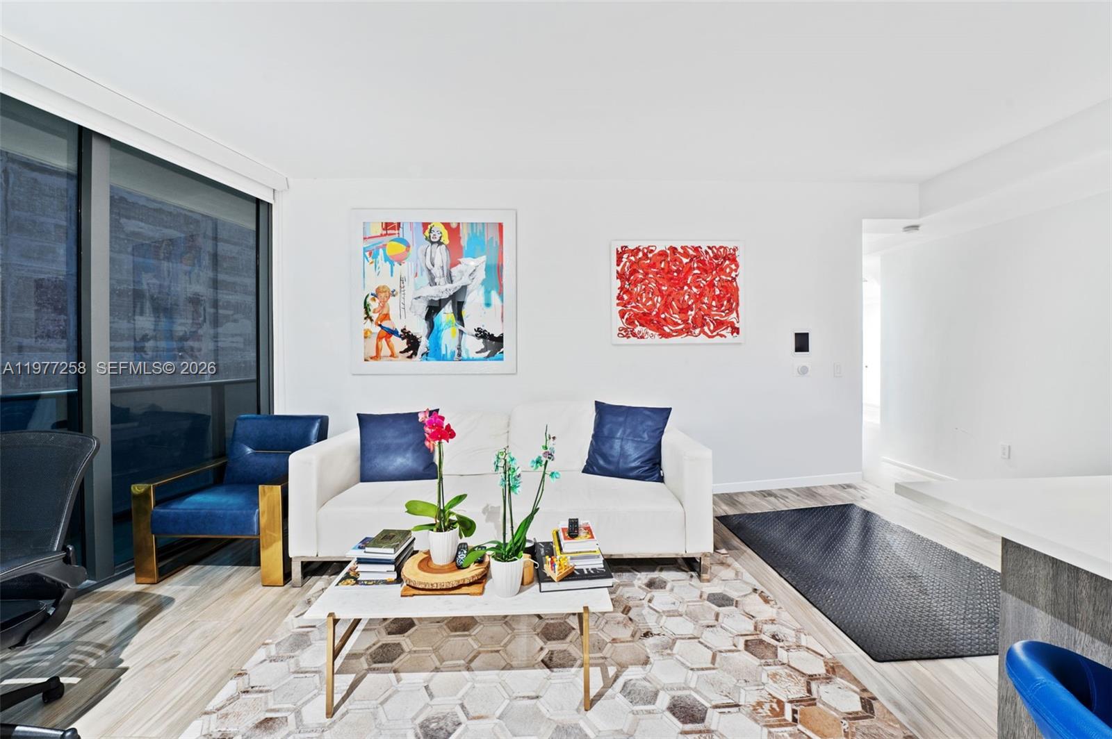 A modern living room features a white sofa, blue accent chair, and colorful wall art — 801 S Miami Ave # 2705, Miami FL 33130, MIAMI, FL