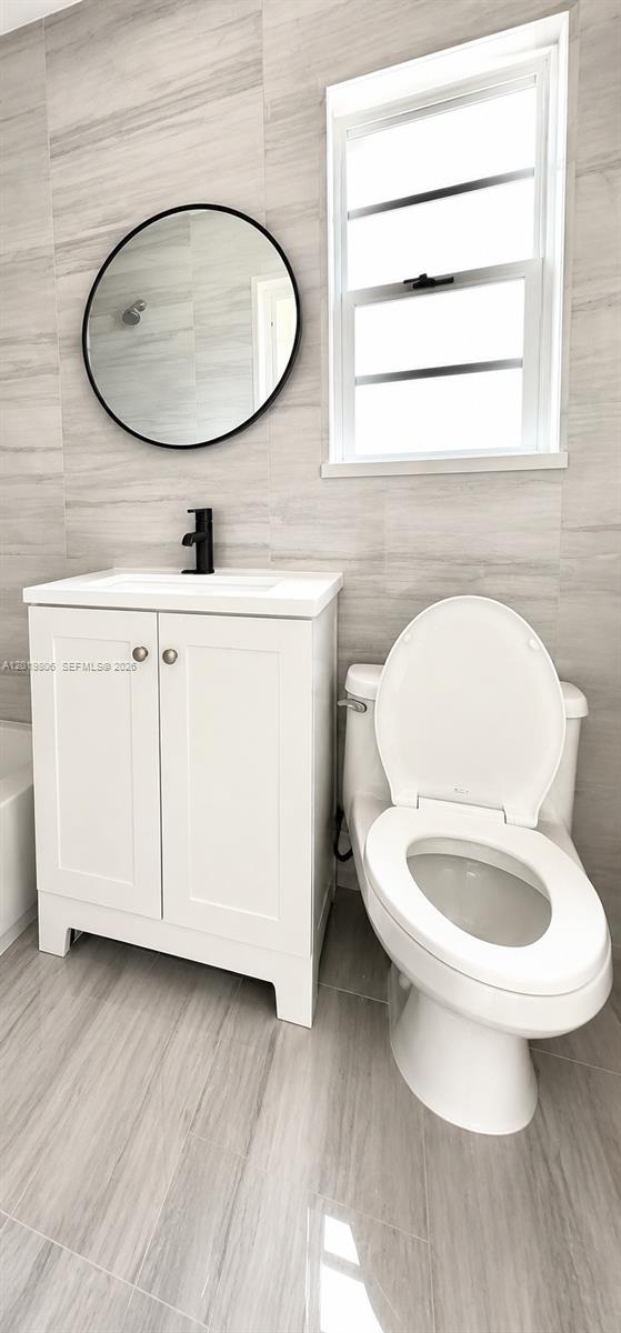 A bathroom features a white vanity, a round black-framed mirror, and light gray tile walls — 612 NW 1st Ave # 00, Hallandale Beach FL 33009, HALLANDALE BEACH, FL