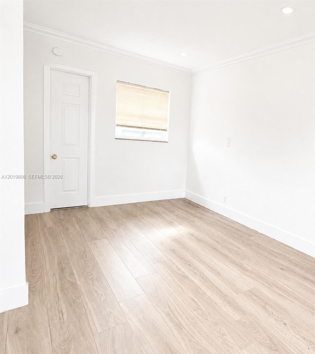 An empty room features white walls, light wood-look flooring, a single window, and a door — 612 NW 1st Ave # 00, Hallandale Beach FL 33009, HALLANDALE BEACH, FL