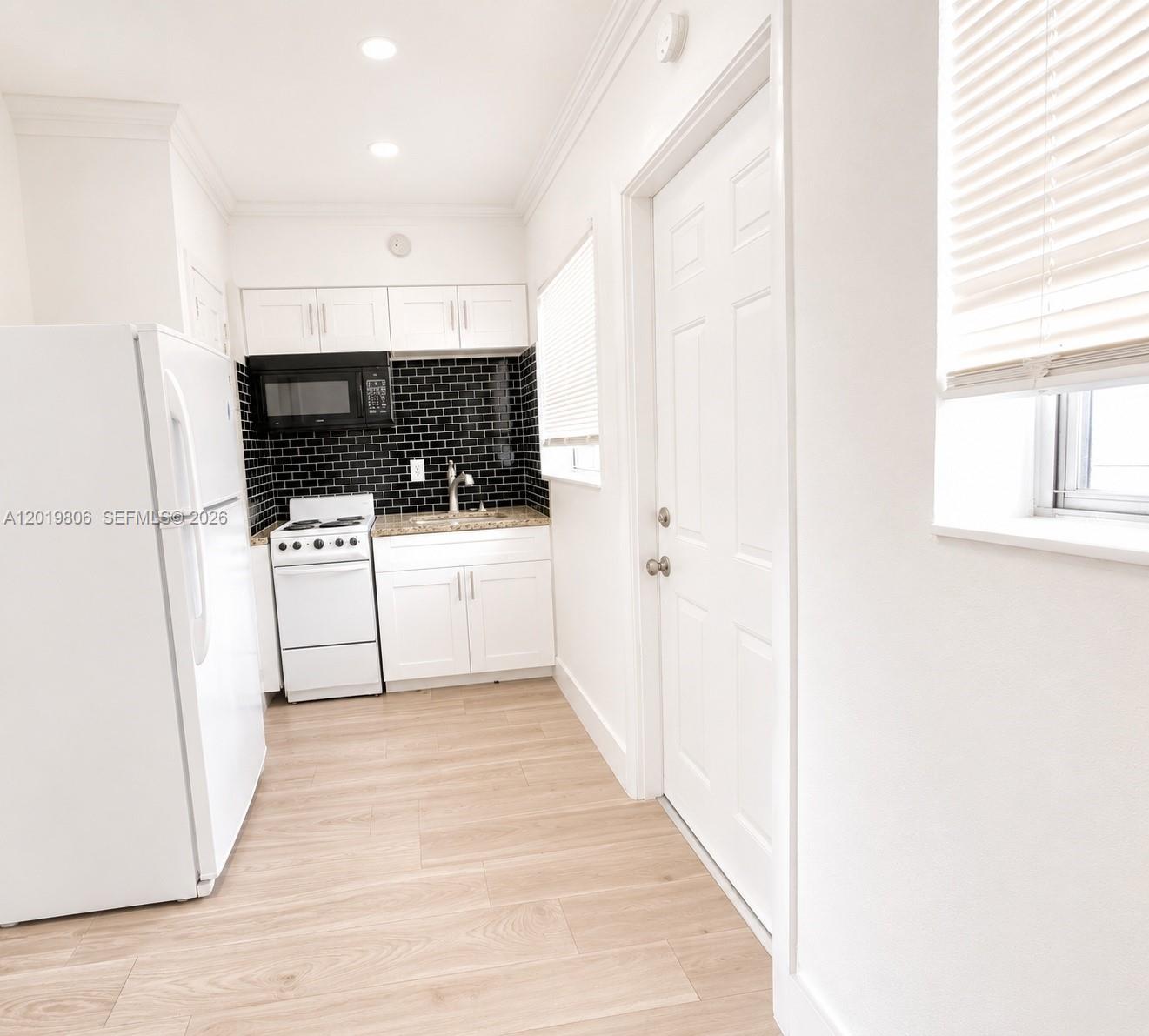 A small kitchen features white cabinets, a black tiled backsplash, and light wood-look flooring — 612 NW 1st Ave # 00, Hallandale Beach FL 33009, HALLANDALE BEACH, FL