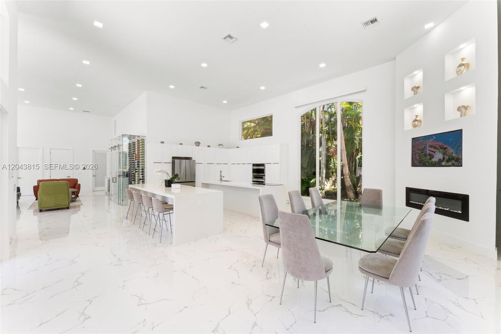 A modern, open-concept kitchen and dining area features white cabinetry, marble flooring, and glass furniture — 2673 NW 64th Blvd, Boca Raton FL 33496, BOCA RATON, FL