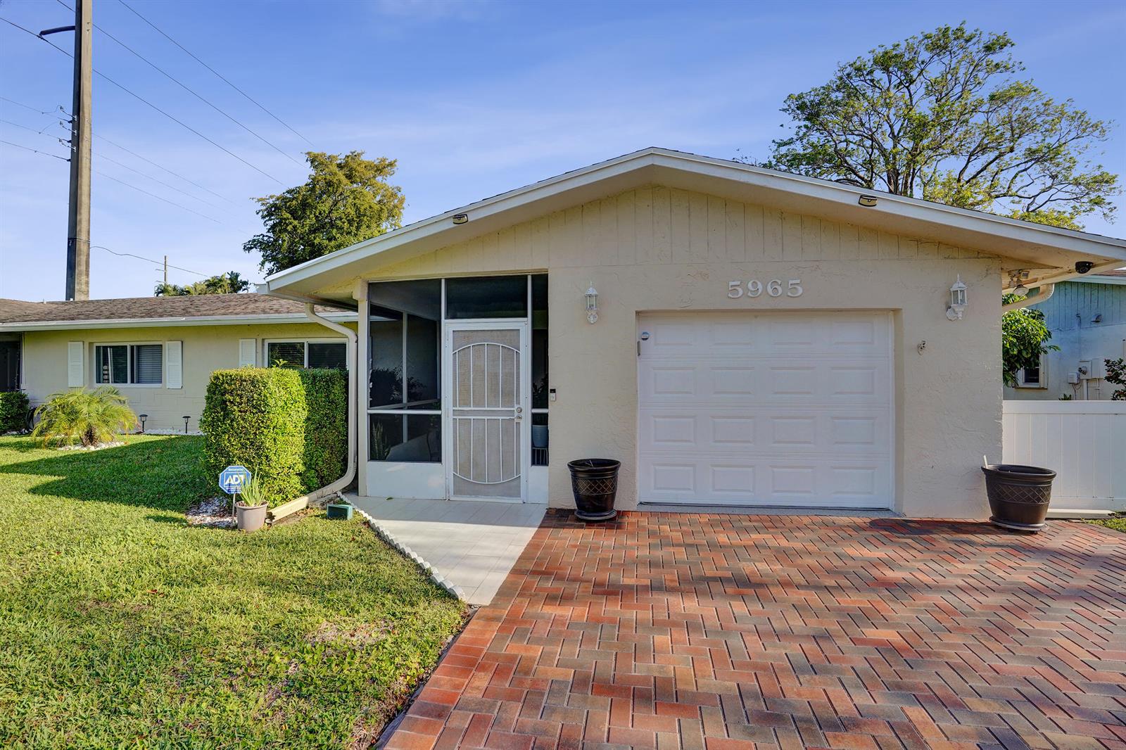 A single-story house features a brick driveway, a garage, and a screened-in front entryway — 5965 Los Alamos Lane, Delray Beach FL 33484, DELRAY BEACH, FL