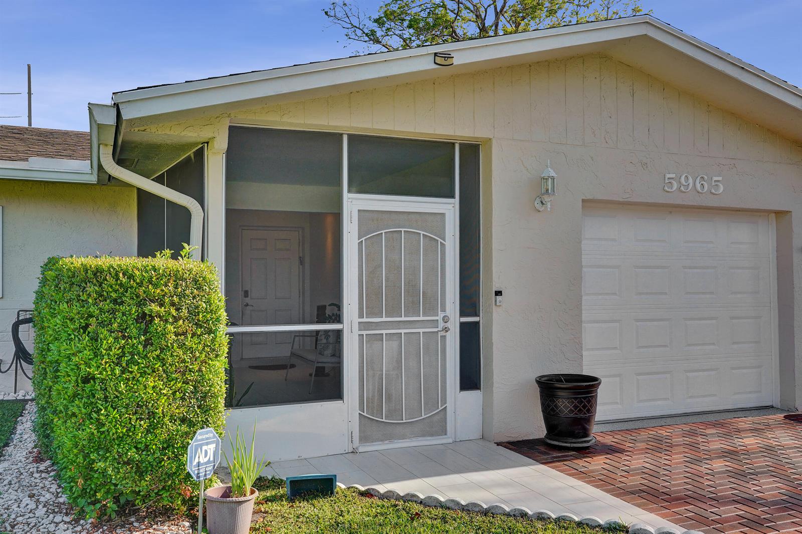 The exterior of a house features a screened-in entryway, a garage, and a brick driveway — 5965 Los Alamos Lane, Delray Beach FL 33484, DELRAY BEACH, FL