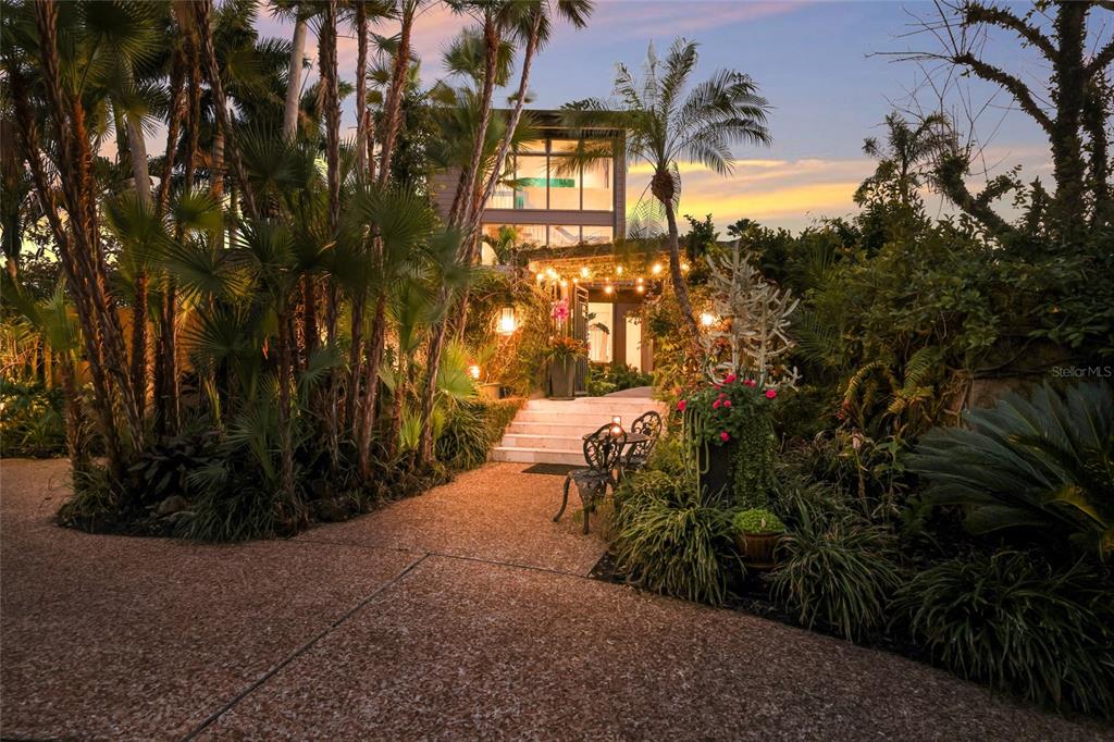 A landscaped path leads to the entrance of a modern home surrounded by palm trees — 608 87TH STREET COURT NW, BRADENTON, FL