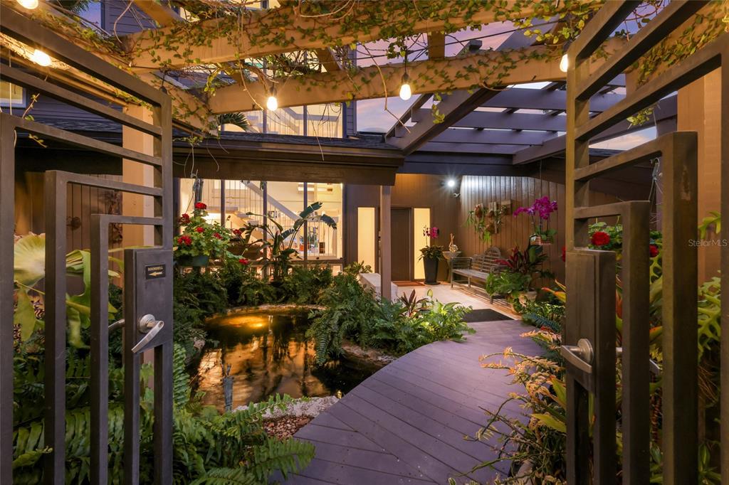 A wooden walkway crosses a koi pond leading to the entrance of a modern home — 608 87TH STREET COURT NW, BRADENTON, FL