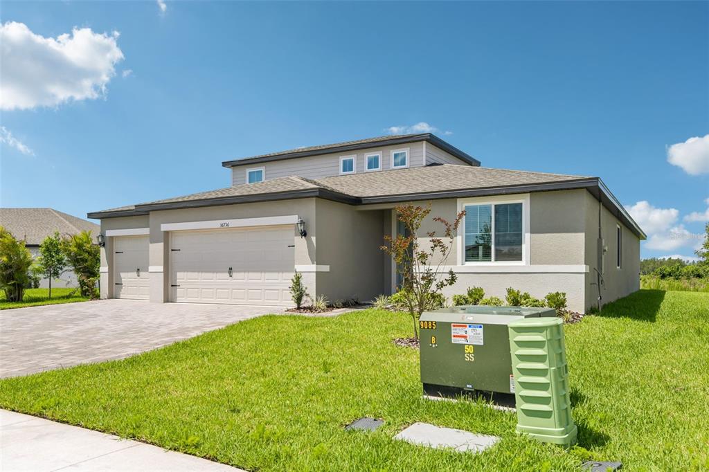 A single-story house with a three-car garage and a green utility box in the yard — 36736 MELSTONE WAY, ZEPHYRHILLS, FL