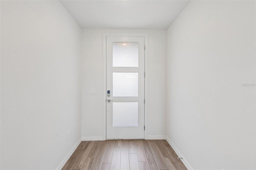 A bright entryway features white walls, wood-look tile flooring, and a modern door with glass panels — 36736 MELSTONE WAY, ZEPHYRHILLS, FL