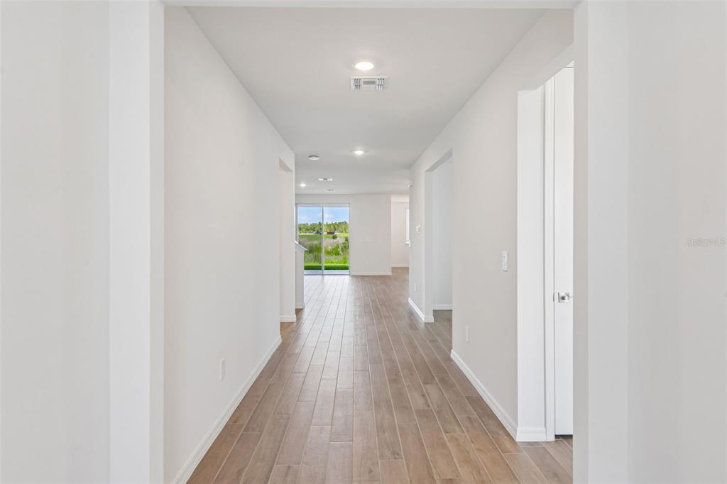 A long hallway with light wood-look tile flooring leads to a glass sliding door — 36736 MELSTONE WAY, ZEPHYRHILLS, FL
