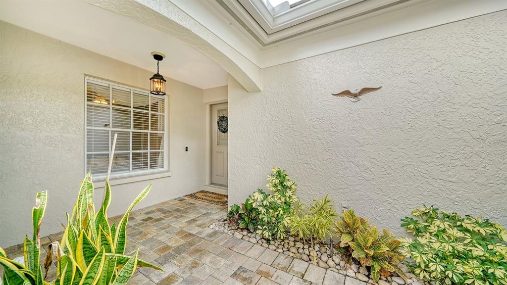 A paved entryway features a front door, a window, and a garden bed with various plants — 4419 OAKLEY GREENE UNIT 19, SARASOTA, FL