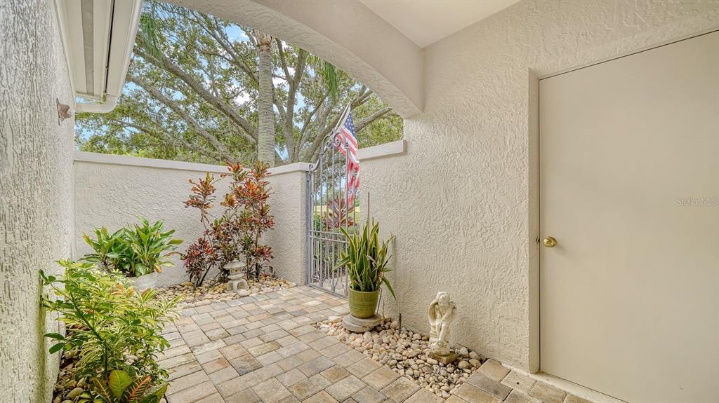 A paved courtyard entrance features a metal gate, potted plants, and a plain beige door — 4419 OAKLEY GREENE UNIT 19, SARASOTA, FL