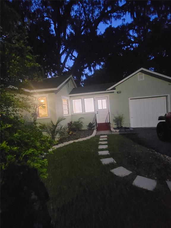 A light green house with a white garage door and a stone walkway at dusk — 5651 ORANGE GROVE AVENUE, NEW PORT RICHEY, FL