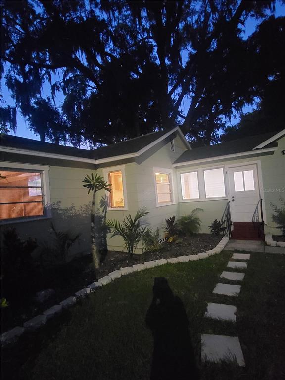A light green house exterior at dusk with a stone walkway and large oak trees — 5651 ORANGE GROVE AVENUE, NEW PORT RICHEY, FL