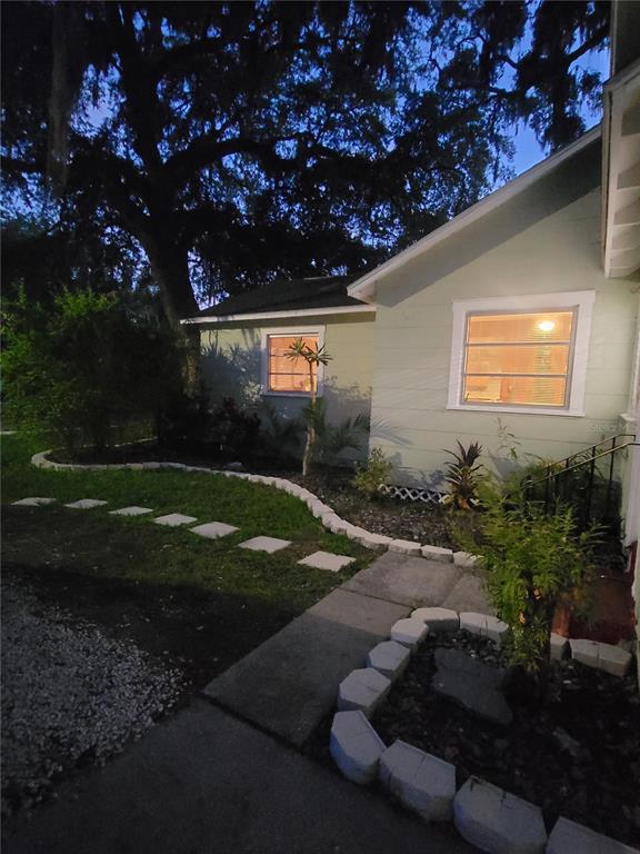 A light green house exterior at dusk features a stone-bordered garden and a concrete walkway — 5651 ORANGE GROVE AVENUE, NEW PORT RICHEY, FL