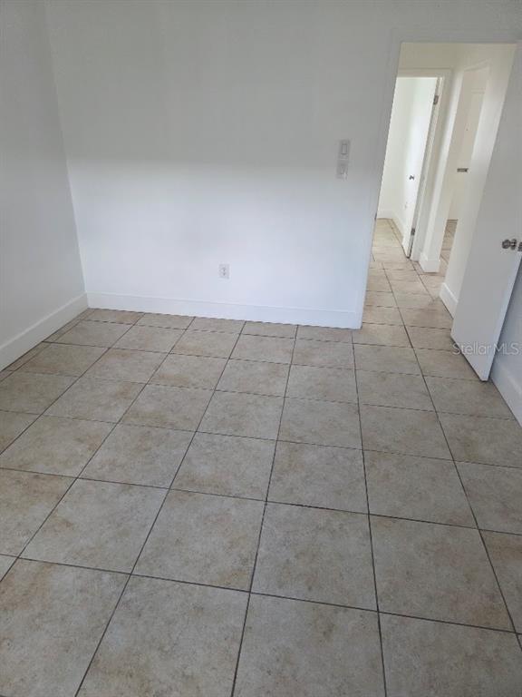 An empty room with light-colored square floor tiles and white walls leads to a hallway — 4994 JONQUIL PLACE N UNIT 278, PINELLAS PARK, FL