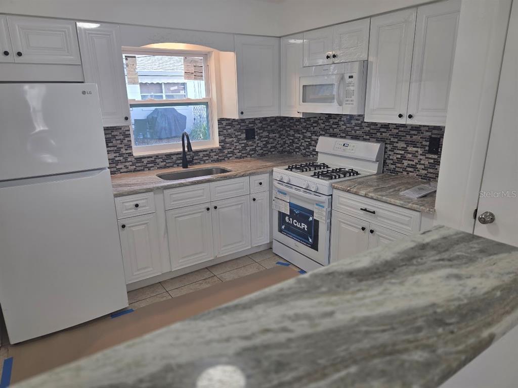 A kitchen features white cabinets, stone countertops, a tiled backsplash, and white appliances — 4994 JONQUIL PLACE N UNIT 278, PINELLAS PARK, FL