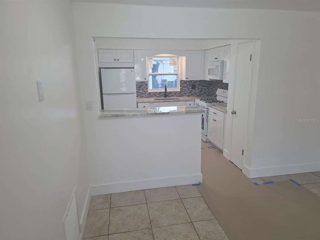A kitchen with white cabinets, a breakfast bar, and tile flooring viewed from an adjacent room — 4994 JONQUIL PLACE N UNIT 278, PINELLAS PARK, FL