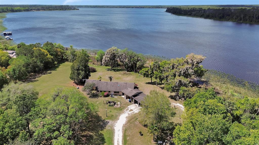 An aerial view shows a single-story house with a driveway situated on a large lakefront lot — 5268 STATE ROAD 11, DE LEON SPRINGS, FL