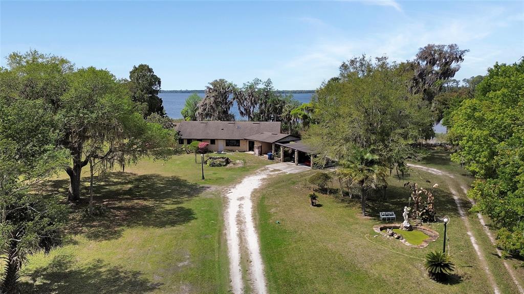 An aerial view shows a single-story house with a carport situated on a grassy lot — 5268 STATE ROAD 11, DE LEON SPRINGS, FL