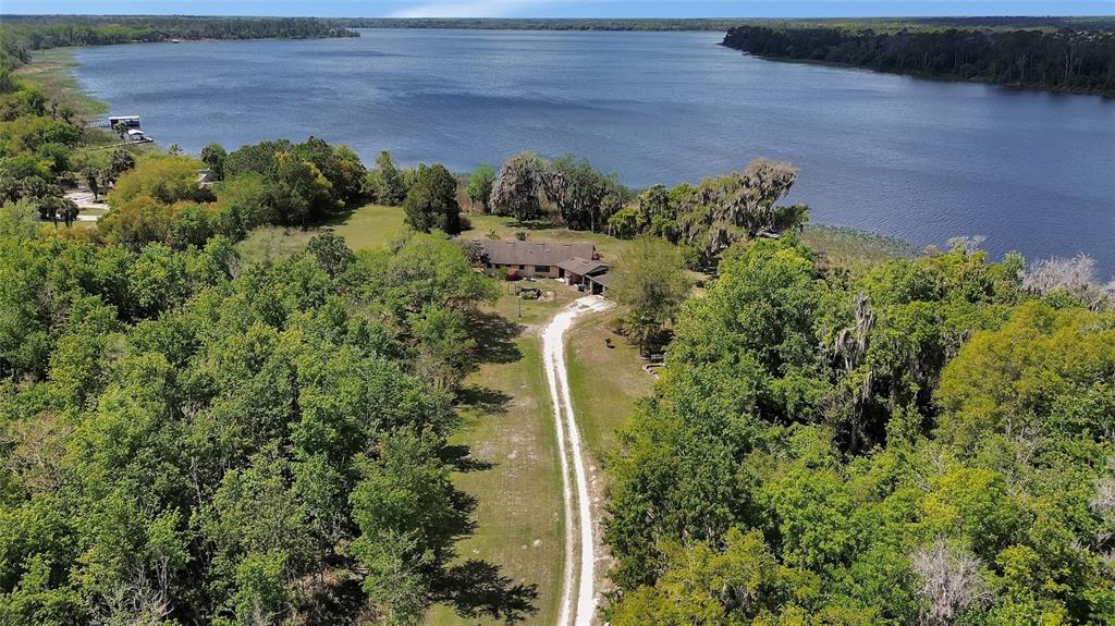 An aerial view shows a house situated on a large, wooded lot beside a lake — 5268 STATE ROAD 11, DE LEON SPRINGS, FL