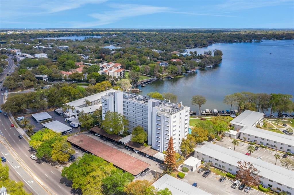 An aerial view shows a multi-story apartment building situated next to a lake and road — 1100 S ORLANDO AVENUE UNIT 306, MAITLAND, FL