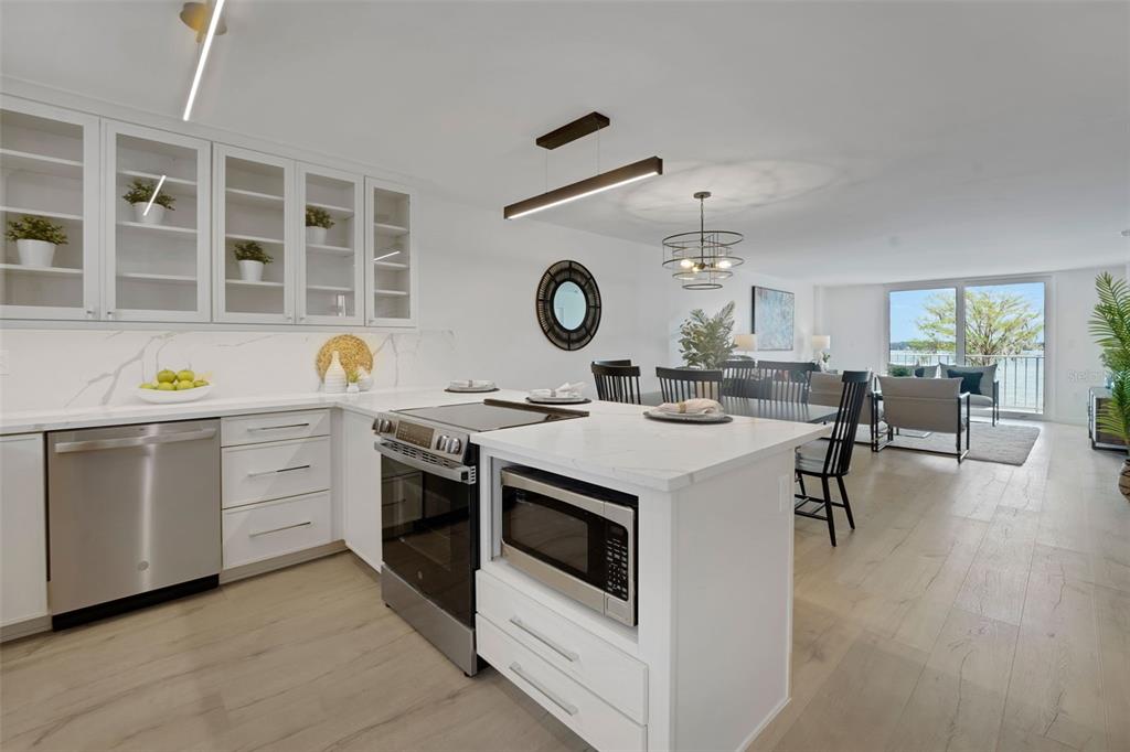 A modern white kitchen with an island and stainless steel appliances opens to a living area — 1100 S ORLANDO AVENUE UNIT 306, MAITLAND, FL