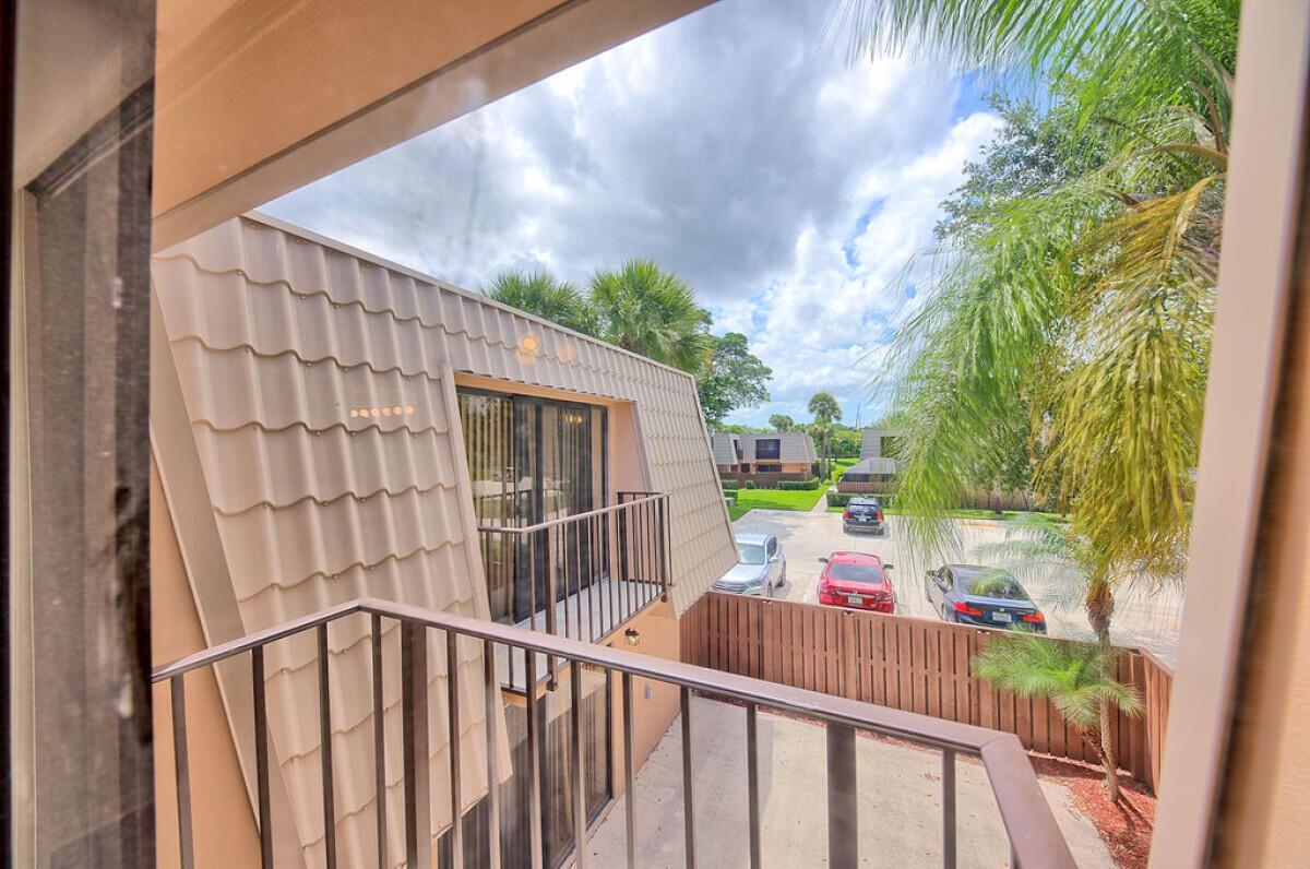 A view from a balcony overlooking a parking lot, palm trees, and a neighboring building — 5731 57th Way # 42a, West Palm Beach FL 33409, WEST PALM BEACH, FL