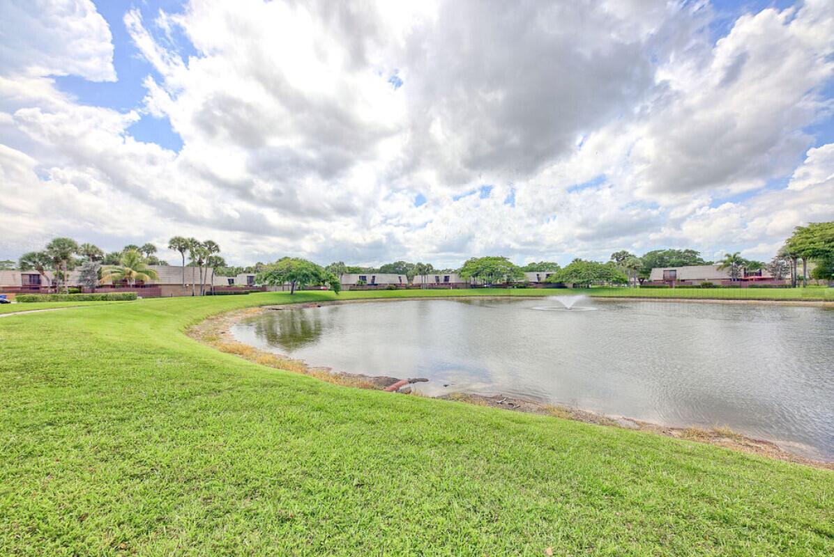 A grassy lawn slopes down to a pond with a fountain in front of residential buildings — 5731 57th Way # 42a, West Palm Beach FL 33409, WEST PALM BEACH, FL