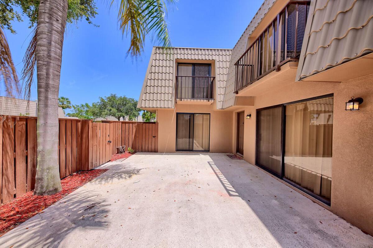 A concrete patio sits outside a two-story tan house with balconies and a wooden fence — 5731 57th Way # 42a, West Palm Beach FL 33409, WEST PALM BEACH, FL