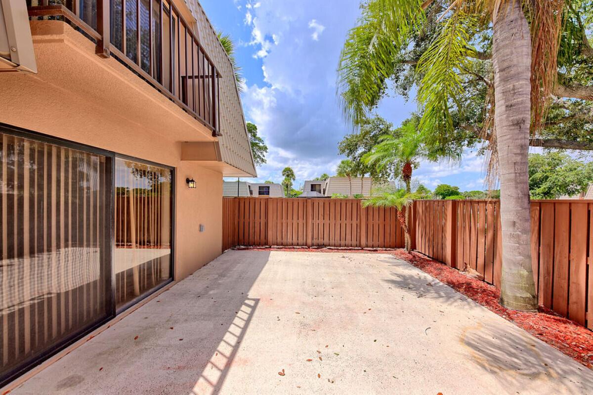 A concrete patio sits beside a building with a balcony and a wooden privacy fence — 5731 57th Way # 42a, West Palm Beach FL 33409, WEST PALM BEACH, FL