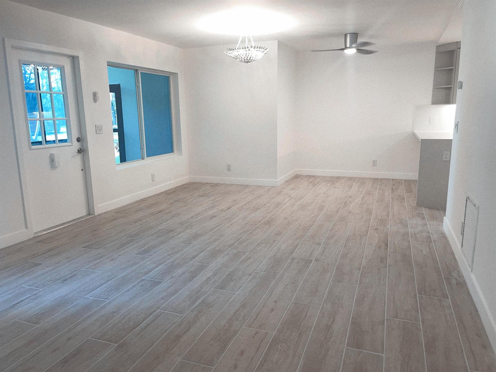 An empty room with light wood-look tile flooring, white walls, a ceiling fan, and chandelier — 5993 La Pinata Boulevard # D1, FL 33463, FL