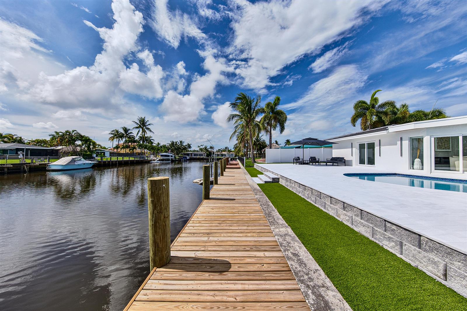 A wooden dock extends along a canal beside a white house with a swimming pool — 411 SE 2nd Avenue, Pompano Beach FL 33060, POMPANO BEACH, FL