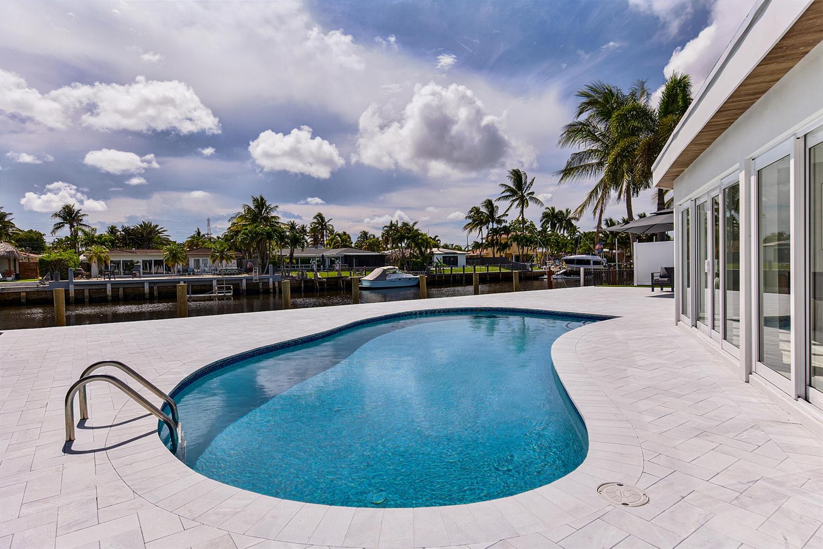 A kidney-shaped swimming pool sits on a tiled patio beside a house overlooking a canal — 411 SE 2nd Avenue, Pompano Beach FL 33060, POMPANO BEACH, FL