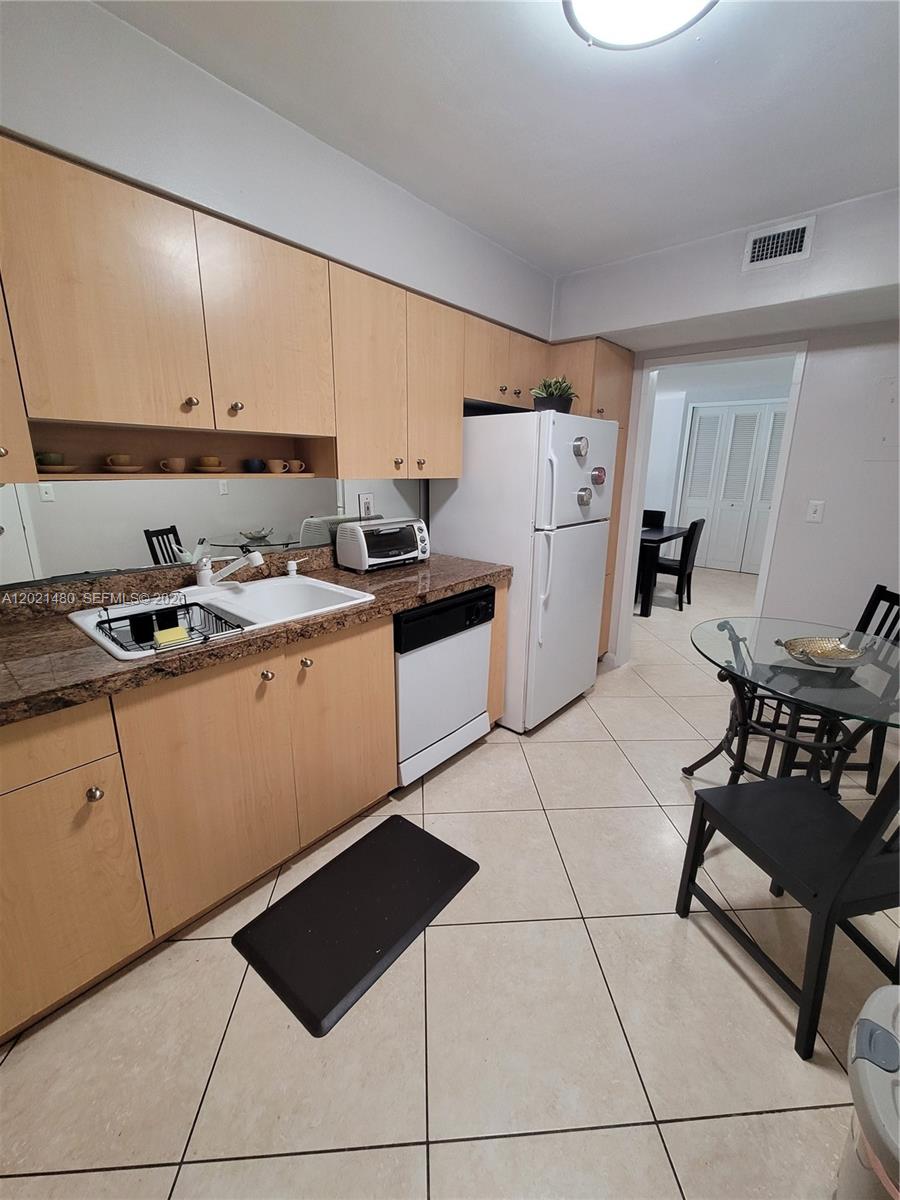 A kitchen features light wood cabinets, granite countertops, white appliances, and a tiled floor — 9195 Collins Ave # 309, Surfside FL 33154, SURFSIDE, FL