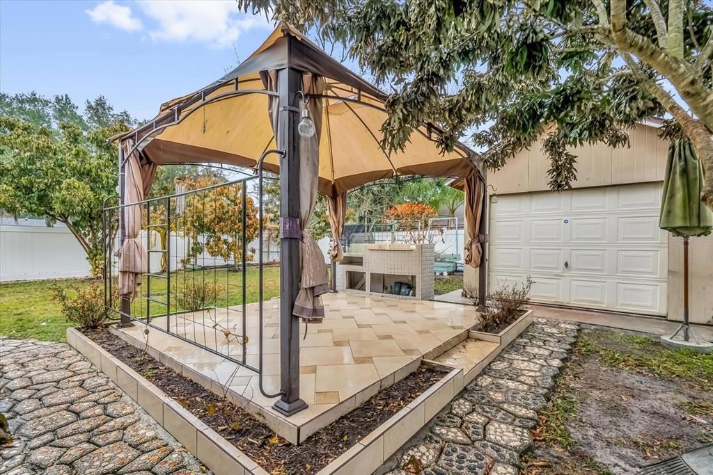 A backyard patio features a metal gazebo, tiled flooring, and a built-in outdoor kitchen — 405 LATONIA STREET, KISSIMMEE, FL