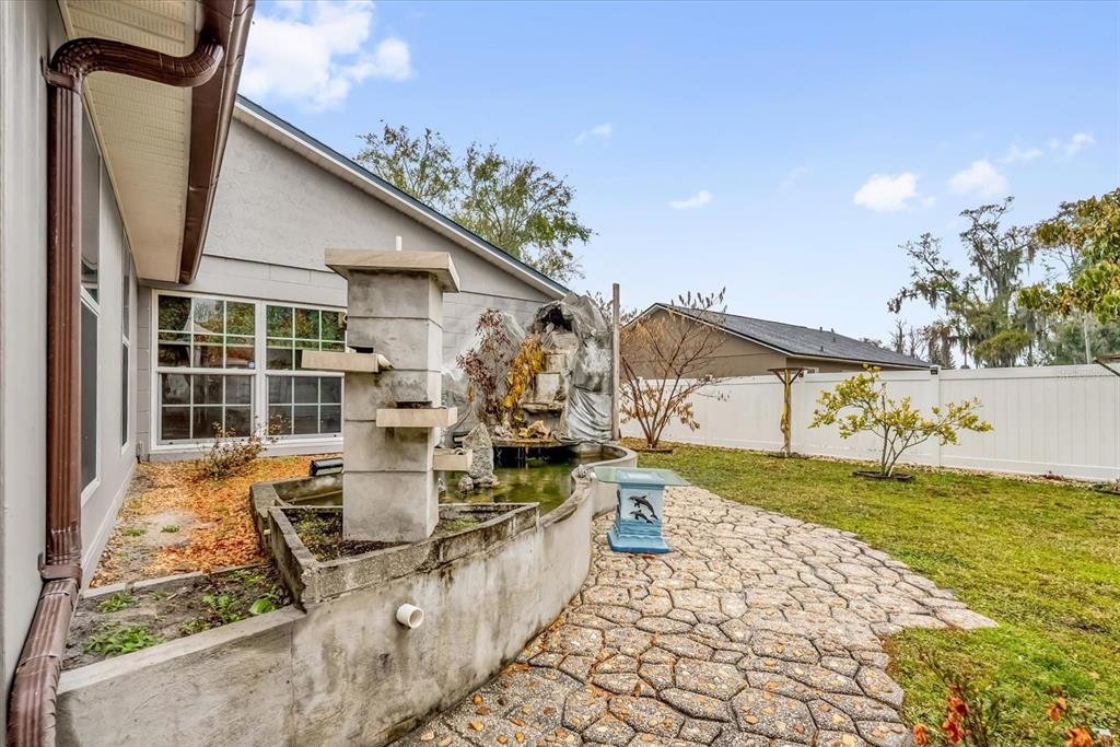 A backyard features a concrete fountain, a stone patio, and a white privacy fence — 405 LATONIA STREET, KISSIMMEE, FL