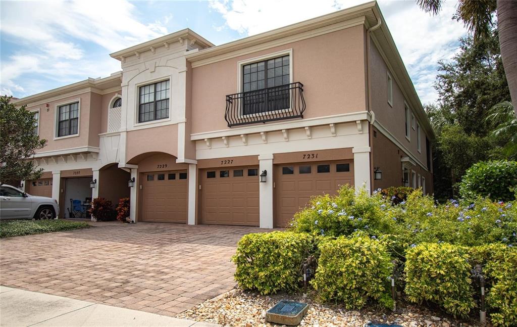 A multi-unit townhouse exterior features tan stucco walls, brown garage doors, and a paved driveway — 7231 HAMILTON ROAD, BRADENTON, FL