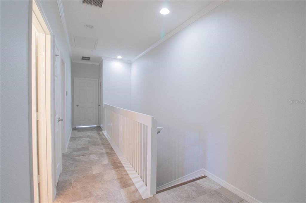 A hallway with tiled flooring, white walls, and a white wooden railing overlooking a staircase — 7231 HAMILTON ROAD, BRADENTON, FL