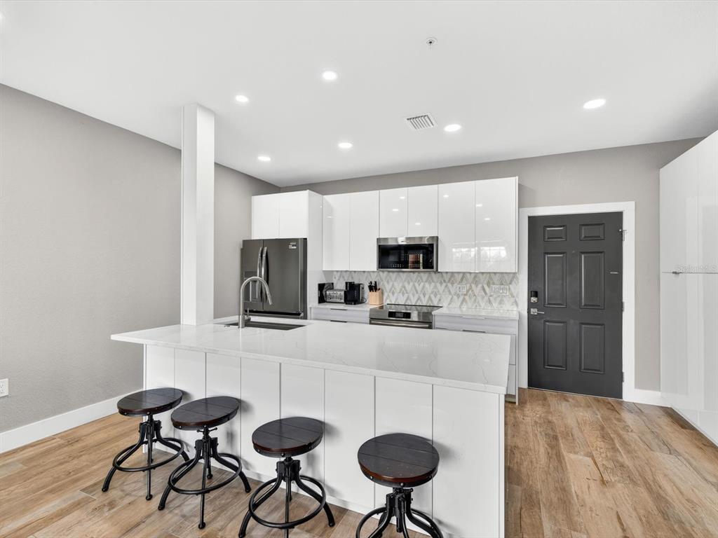 A modern kitchen features white cabinets, a quartz-topped island with bar stools, and wood flooring — 5000 CULBREATH KEY WAY UNIT 9-116, TAMPA, FL